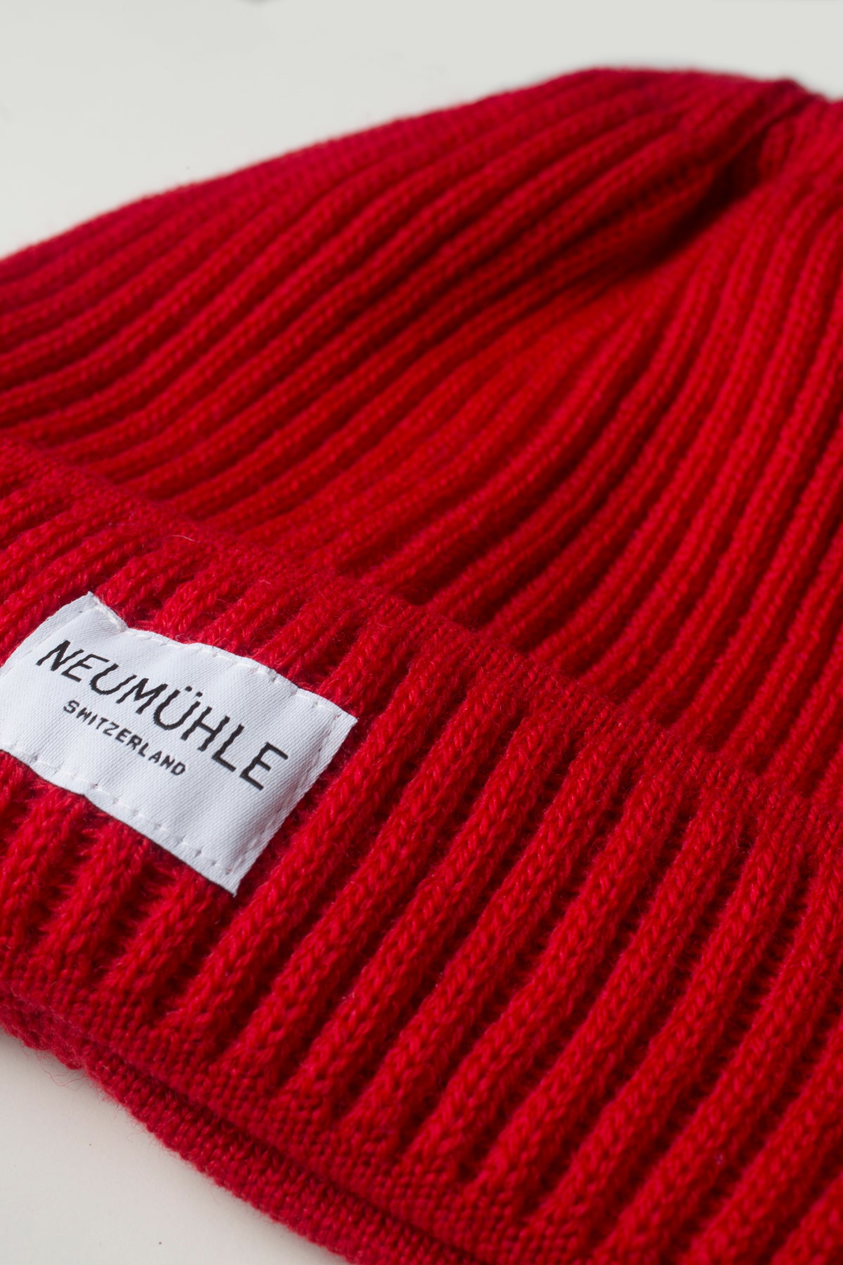 Logo-Detail der nachhaltigen Mütze Elbe aus Bio-Merinowolle von Neumühle in Rot, lokal in Deutschland gefertigt